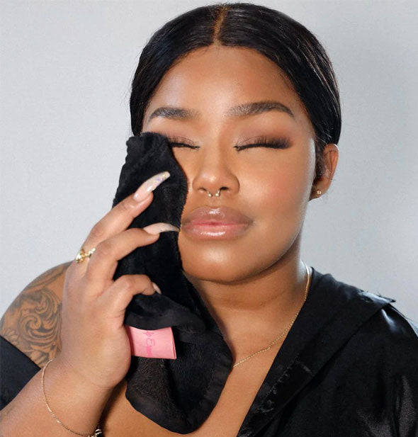 Model with eyes closed touches face with a black MakeUp Eraser