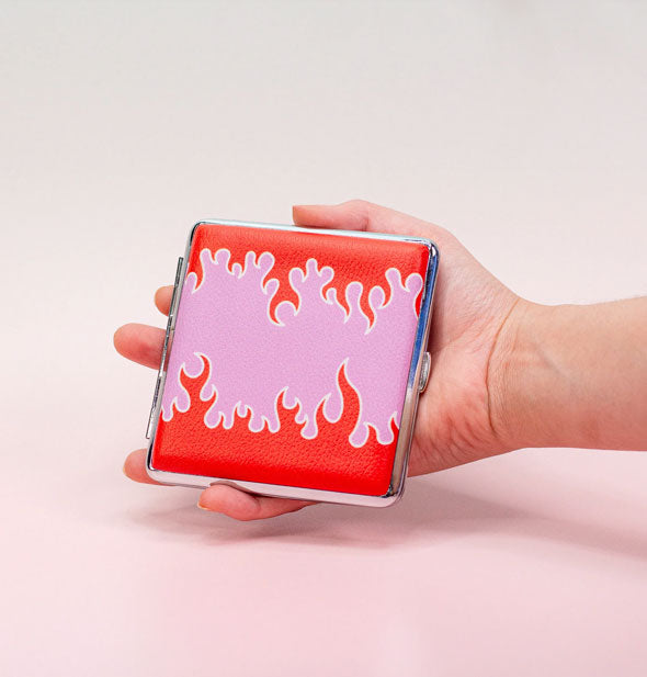 Model's hand holds a square cigarette case with pink and red flame design and silver edge