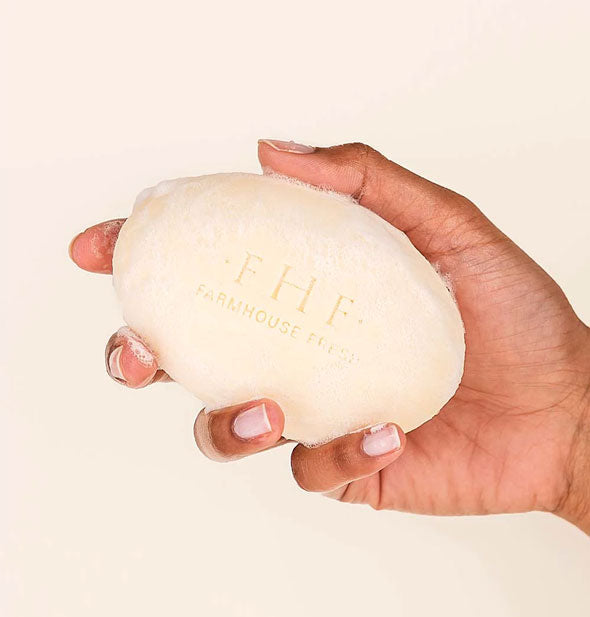 Model's hand holds a slightly lathered bar of FarmHouse Fresh soap