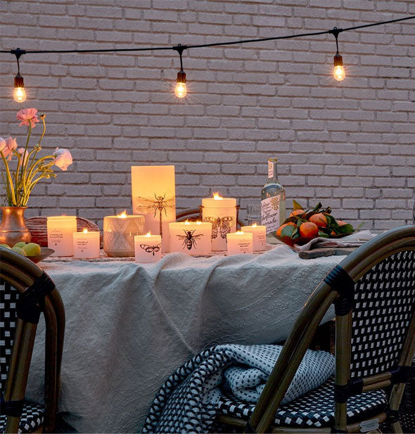 Lit-from-within white insect candles on an outdoor table setting against a brick backdrop
