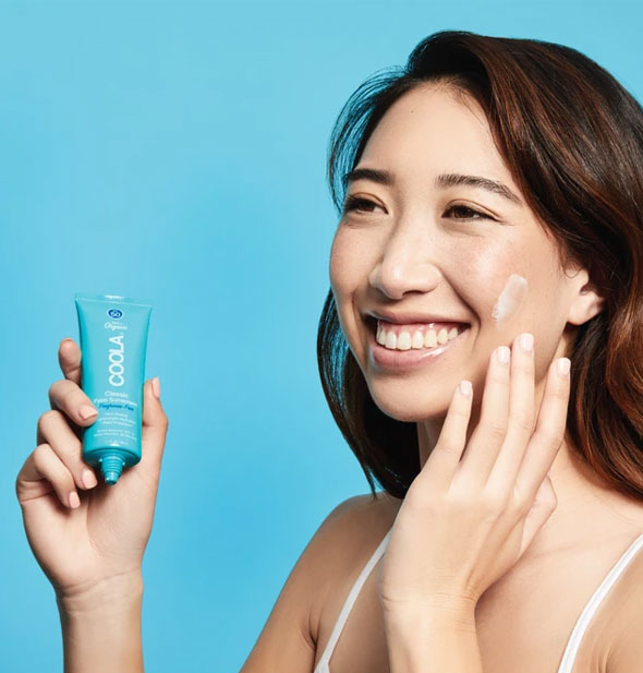 A model applies COOLA Classic Face Sunscreen to cheek