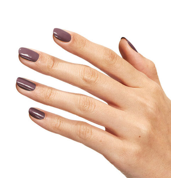 Model's hand wears a shade of earthy brownish-purple nail polish