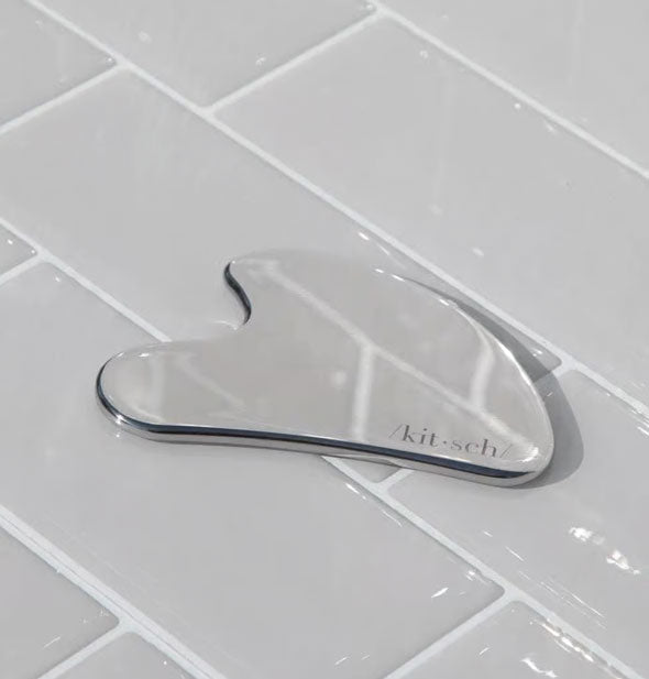 Reflective Stainless Steel Gua Sha by Kitsch on gray tile