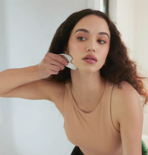 Model demonstrates use of the Kitsch Stainless Steel Gua Sha facial massager on jawline