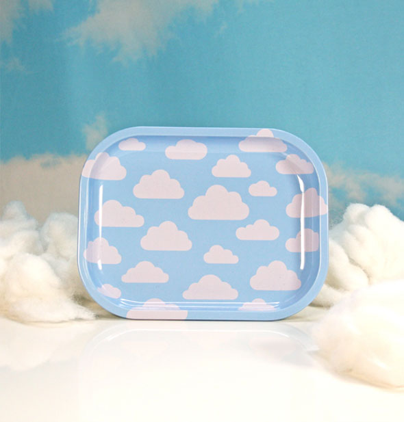Square blue tray with rounded corners has all-over puffy white cloud print and rests against white fluff on a blue backdrop