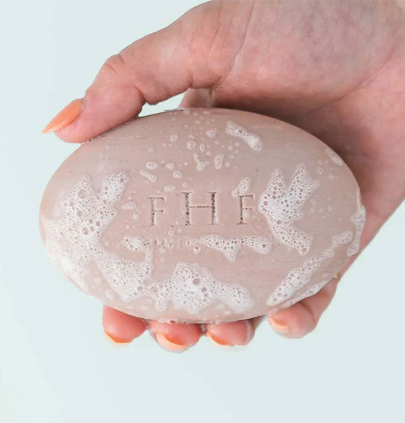 Model's hand holds a sudsy bar of FarmHouse Fresh soap
