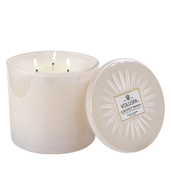 Creamy-colored glass jar candle with three burning wicks and embossed lid set to the side