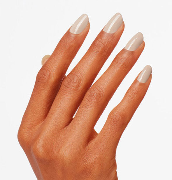 Model's hand wears a light taupe shade of nail polish