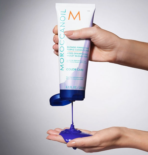 Model dispenses Moroccanoil Blonde Perfecting purple Conditioner from bottle into hand