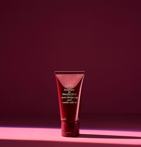 Small burgundy bottle of Oribe Conditioner for Beautiful Color on dark shadowy background