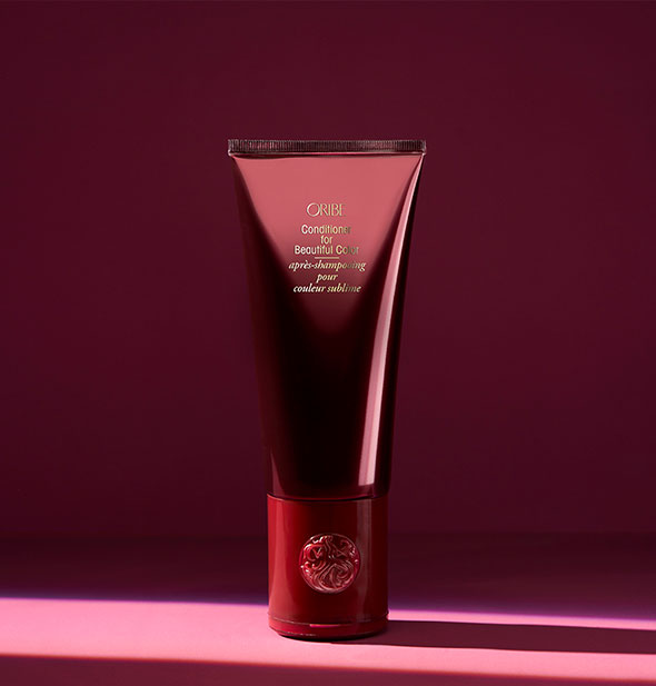 Burgundy bottle of Oribe Conditioner for Beautiful Color on dark shadowy background