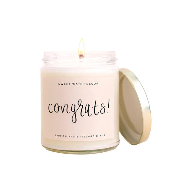 Lit glass jar Sweet Water Decor candle with metal lid and label that says, "Congrats!" in black script