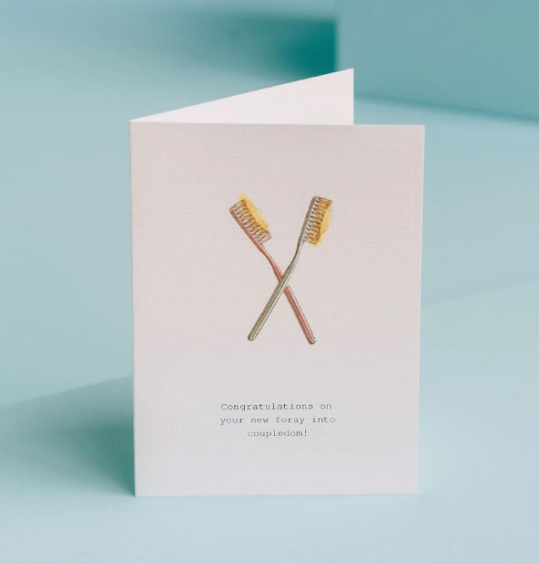 White greeting card with two toothbrushes illustration says, "Congratulations on your new foray into coupledom!"