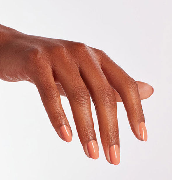 Model's hand wears a peachy-pink coral shade of nail polish