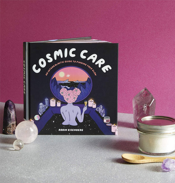 Cosmic Care sits on a tabletop with crystals, orbs, and bath salt jar with wooden spoon