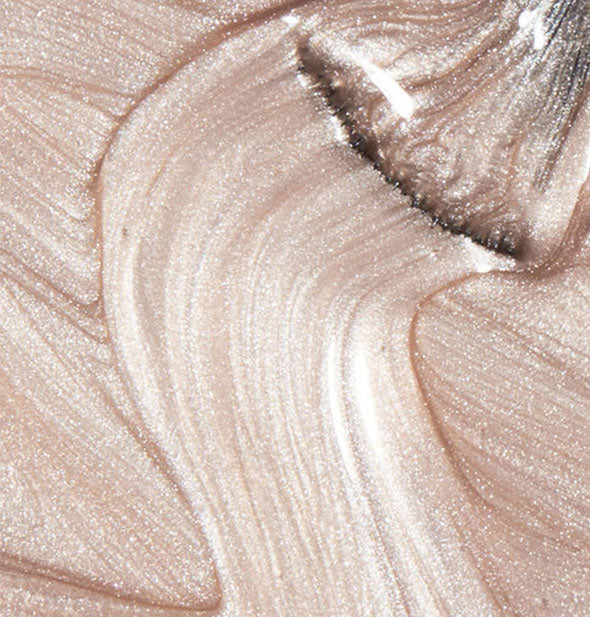 Closeup of shimmery champagne-colored nail polish with brush tip swiped through it