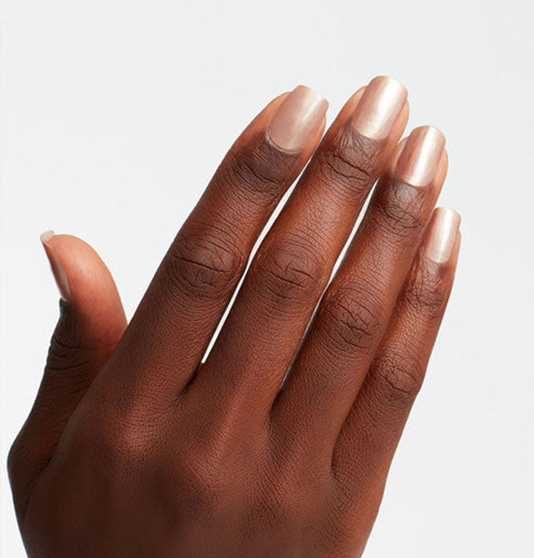 Model's hand wears an iridescent shade of champagne-colored nail polish