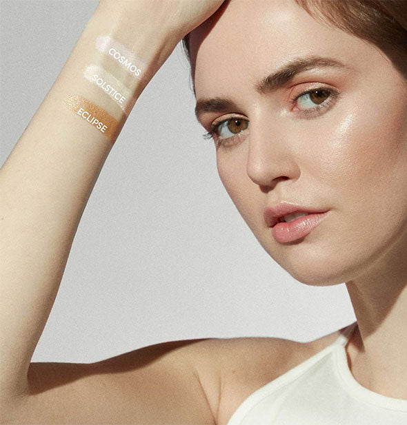 Model with light skin tone raises arm painted with three labeled shades of Jane Iredale Glow Time Highlighter Stick