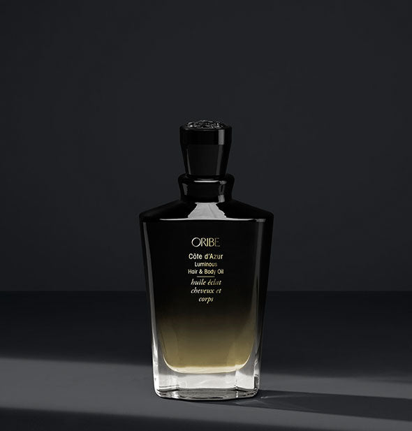 Gold-to-black bottle of Oribe Côte d'Azur Luminous Hair & Body Oil on dark gray background