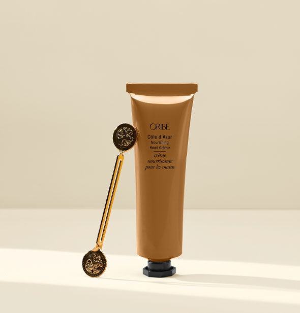 Bronze-colored tube of Oribe Côte d'Azur Nourishing Hand Crème with double-ended twist key resting against it