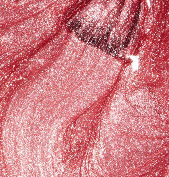 Closeup of shimmery pink nail polish with brush tip drawn through it