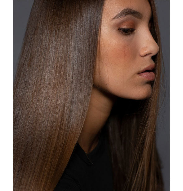 Model with sleek, straight hairstyle demonstrates results of using IGK Crybaby Anti-Frizz Smoothing Serum