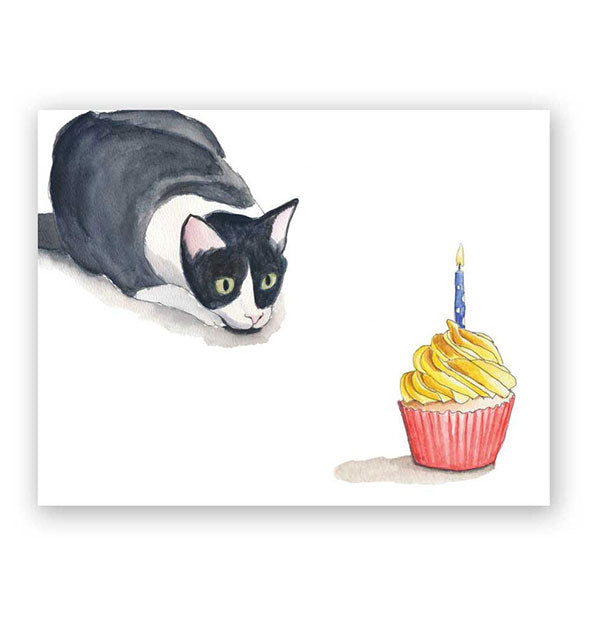 White greeting card features illustration of a black and white cat stalking an iced cupcake in red wrapper with a lit blue candle on top