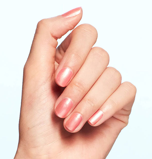 Model's hand wears a shimmery shade of peachy-pink nail polish