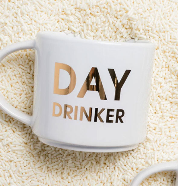 White "Day Drinker" Mug sits on a backdrop of white sprinkles.