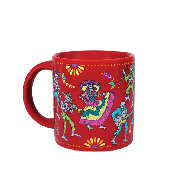 Red coffee mug with illustrations of skeletons in costumes playing instruments and dancing in the theme of Día de los Muertos