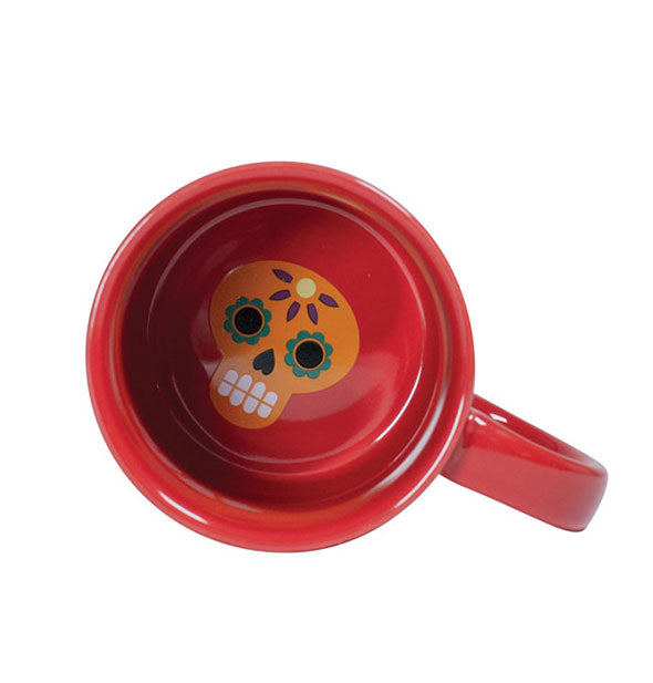 Top view of red coffee mug shows a colorful Día de los Muertos skull in th ebottom