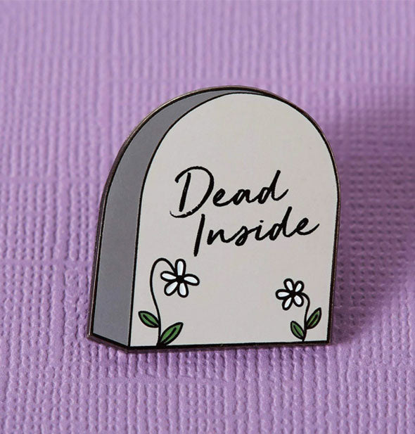 Enamel pin designed to resemble a graveyard headstone says, "Dead Inside" with two daisies below