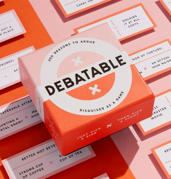 Debatable game box rests on top of sample cards on a red and pink color blocked surface