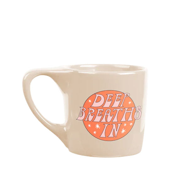 Angular beige coffee mug says, "Deep Breaths In" in pink lettering inside an orange circle with star accents