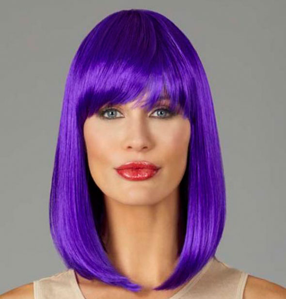 Model wearing a shoulder length, purple wig with bangs.