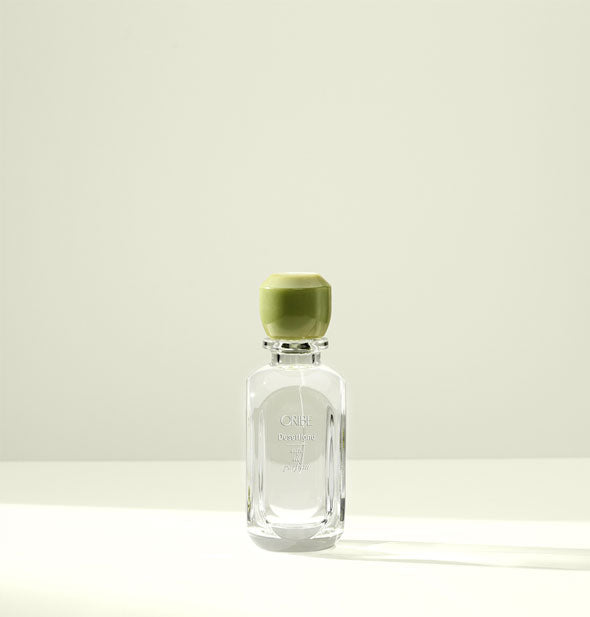 Clear glass bottle of Oribe Desertland Eau de Parfum with green beveled cap