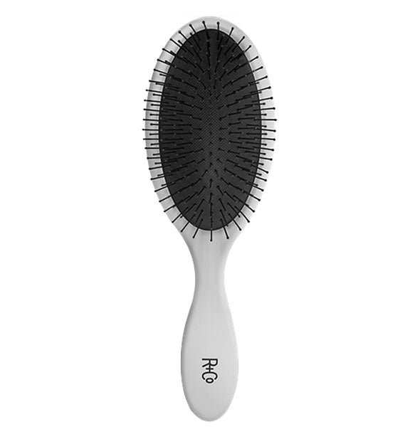 Gray paddle brush with black cushion and bristles and R+Co logo stamped on handle