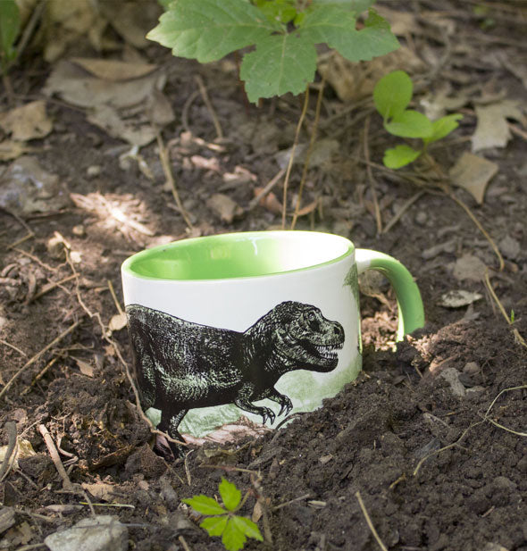 Dinosaur mug partially buried in soil