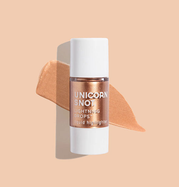 Bottle of Unicorn Snot Lightning Drops Liquid Highlighter in the shade Diva with sample application on a light peach surface