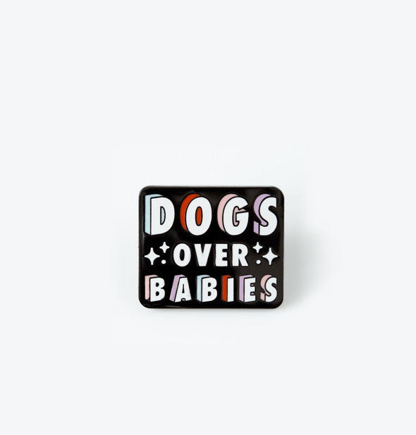 Rectangular black enamel pin with rounded corners says, "Dogs Over Babies" in white lettering with colorful shadow effect and star accents