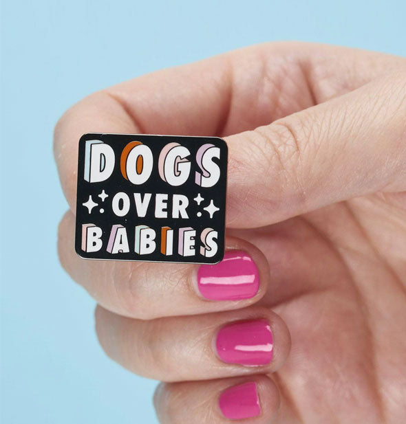 Model's hand holds a Dogs Over Babies enamel pin for size reference