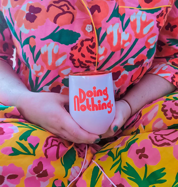 Model holds a Doing Nothing wine tumbler in both hands against bold floral prints