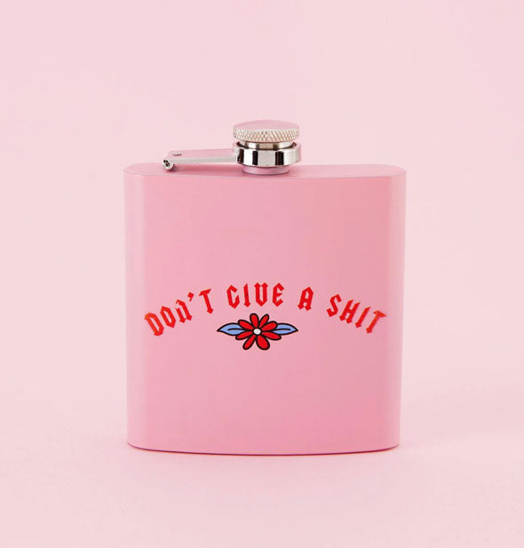 Square pink flask says, "Don't Give a Shit" in red lettering above a flower illustration
