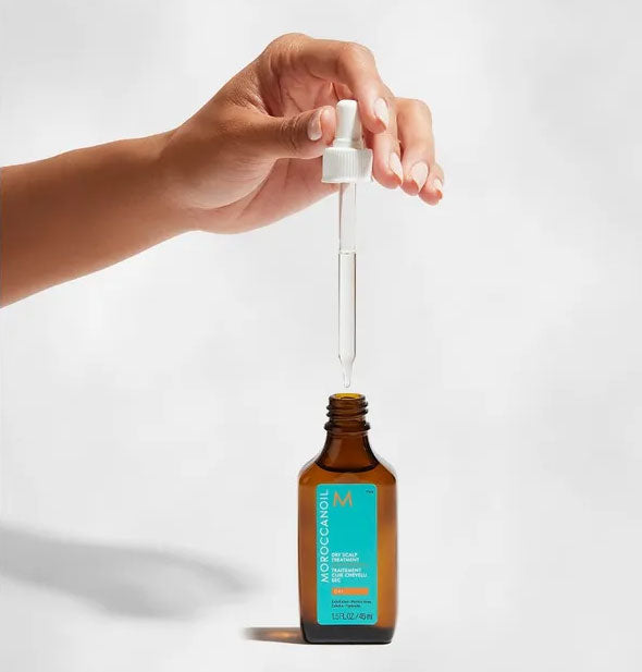 Model's hand lifts the Moroccanoil Dry Scalp Treatment dropper from bottle