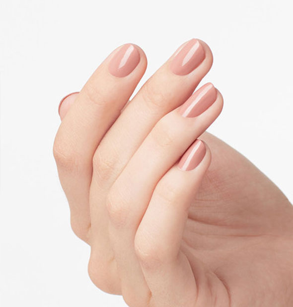 Model's hand wears a pinkish-beige shade of nail polish