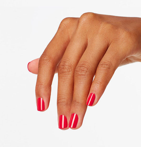 Model's hand wears a shade of reddish pink nail polish