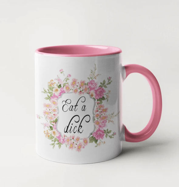 White coffee mug with pink handle and interior says, "Eat a Dick" in decorative script surrounded by pink flowers