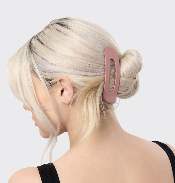 Model wears a large matte pink slotted hair clip in a twisted, messy low chignon style