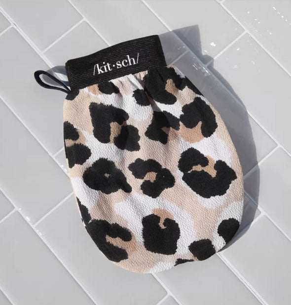 Black, white, and tan leopard print Kitsch exfoliating mitt on a white tiled surface