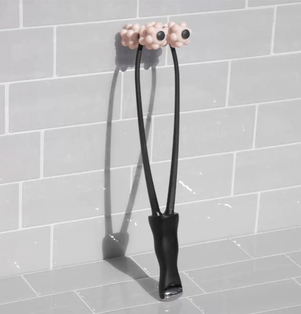 Black and pink facial roller with dual nubby ends rests against a gray tiled wall